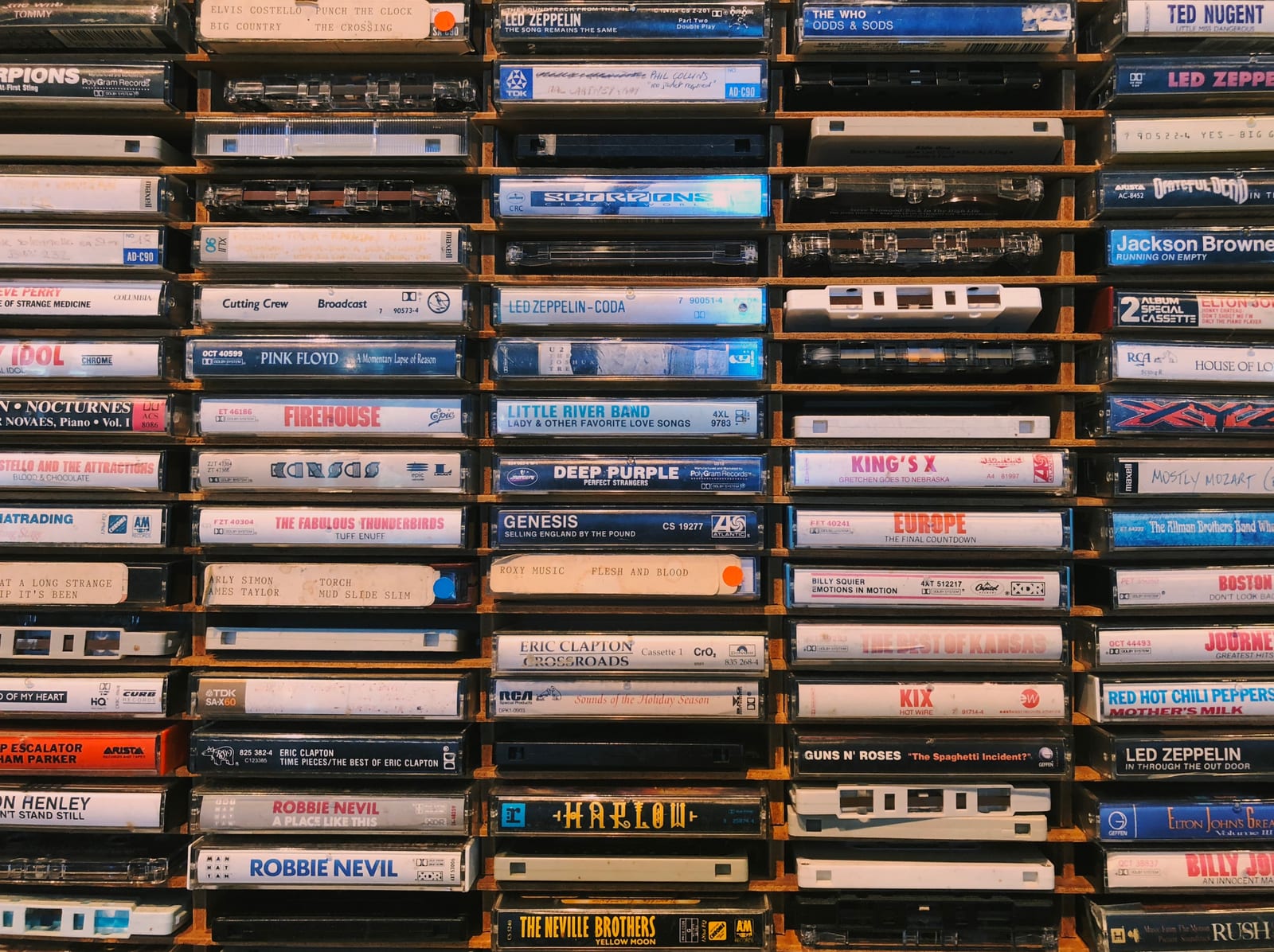 Wall of stacked cassette tapes in wooden shelves, labeled with rock bands like Led Zeppelin, Pink Floyd, and Genesis.